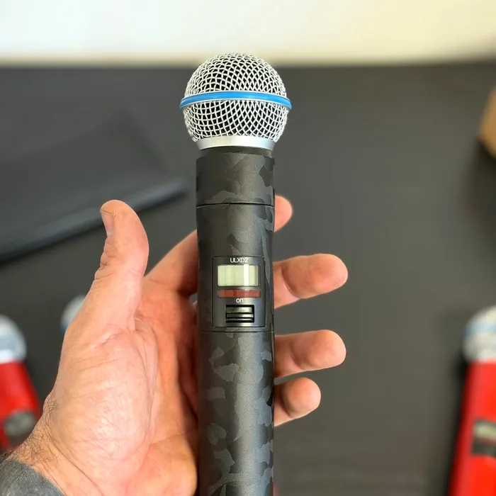 Hand houdt een draadloze Shure ULXD2-microfoon vast, gewrapt in zwarte camouflageprint