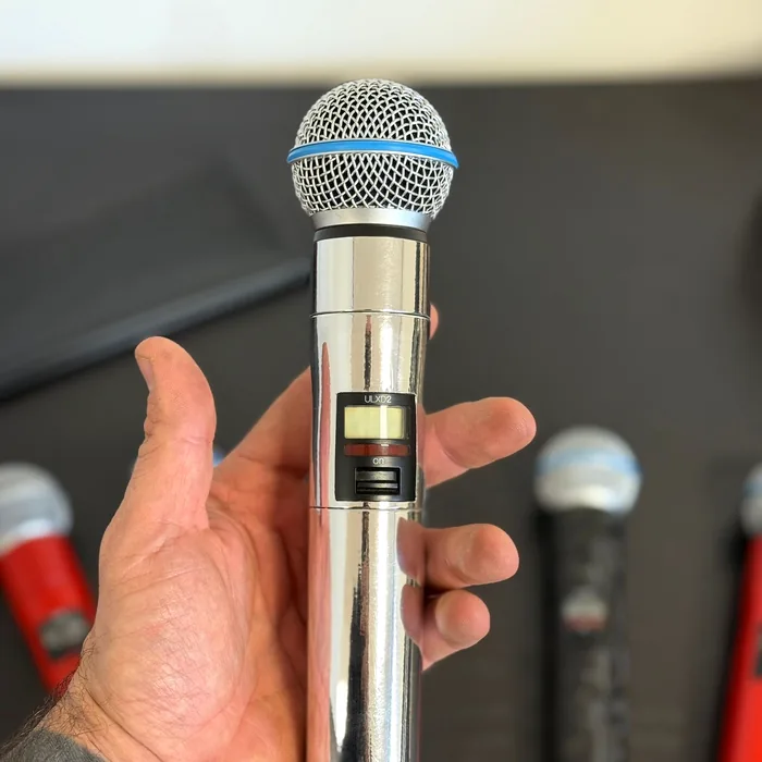 Hand houdt een draadloze Shure-microfoon vast, gewrapt in spiegelend chroom