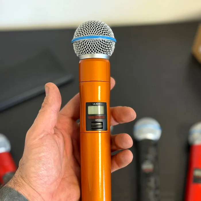 Hand houdt een draadloze Shure-microfoon vast, gewrapt in metallic oranje