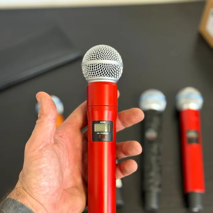 Hand houdt een draadloze Shure-microfoon vast, gewrapt in rood hoogglans