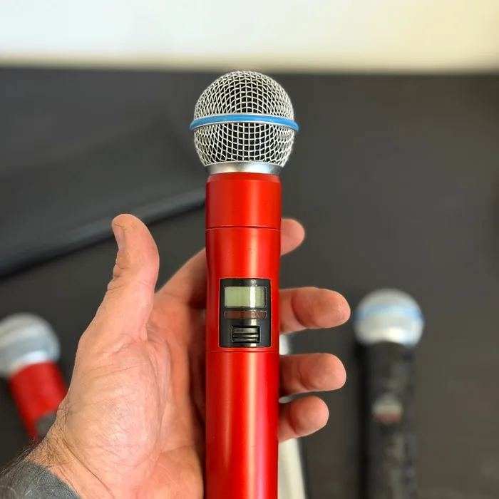 Hand houdt een draadloze Shure-microfoon vast, gewrapt in satijn rood