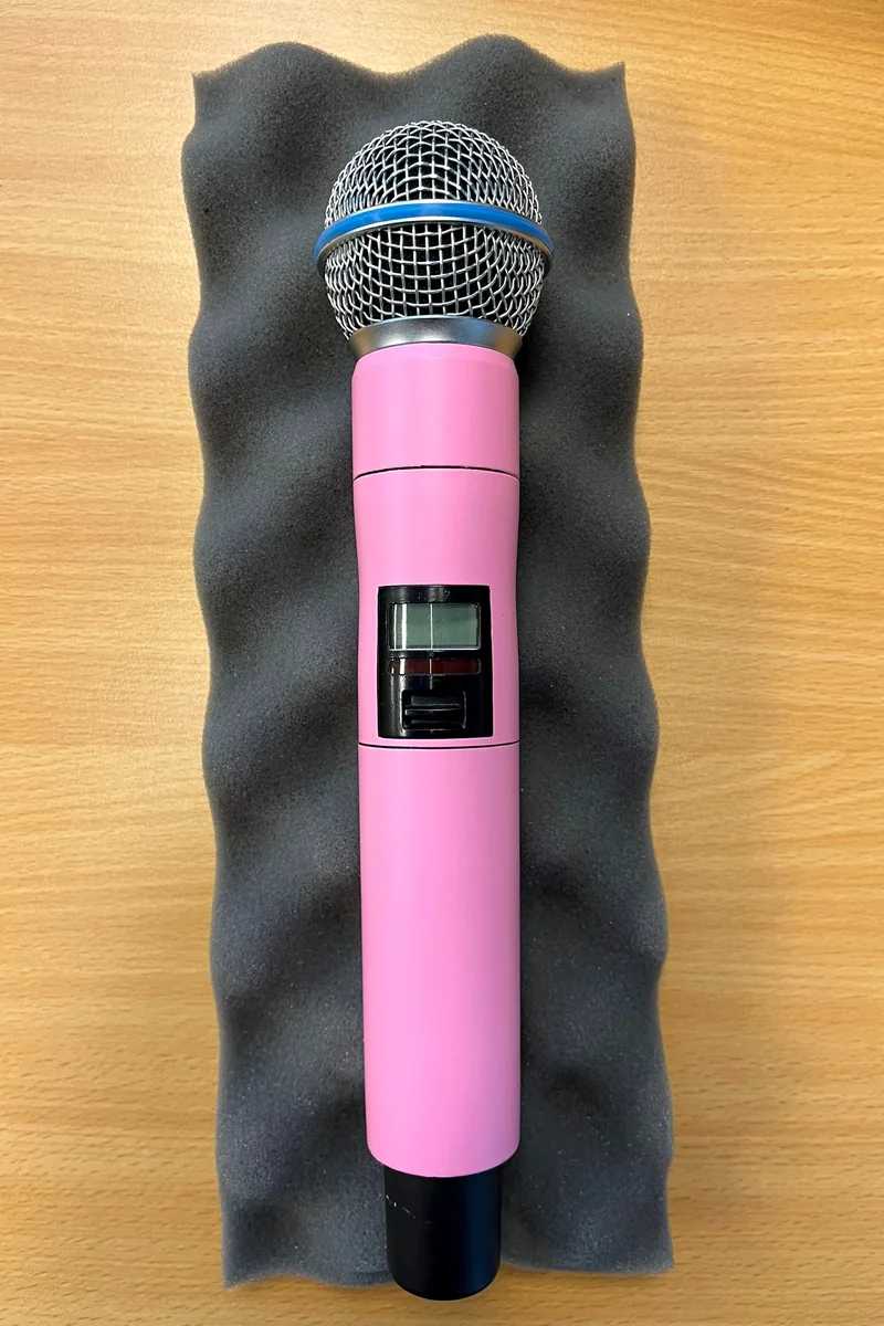 Dezelfde draadloze Shure-microfoon in mat roze, van bovenaf op grijs schuim