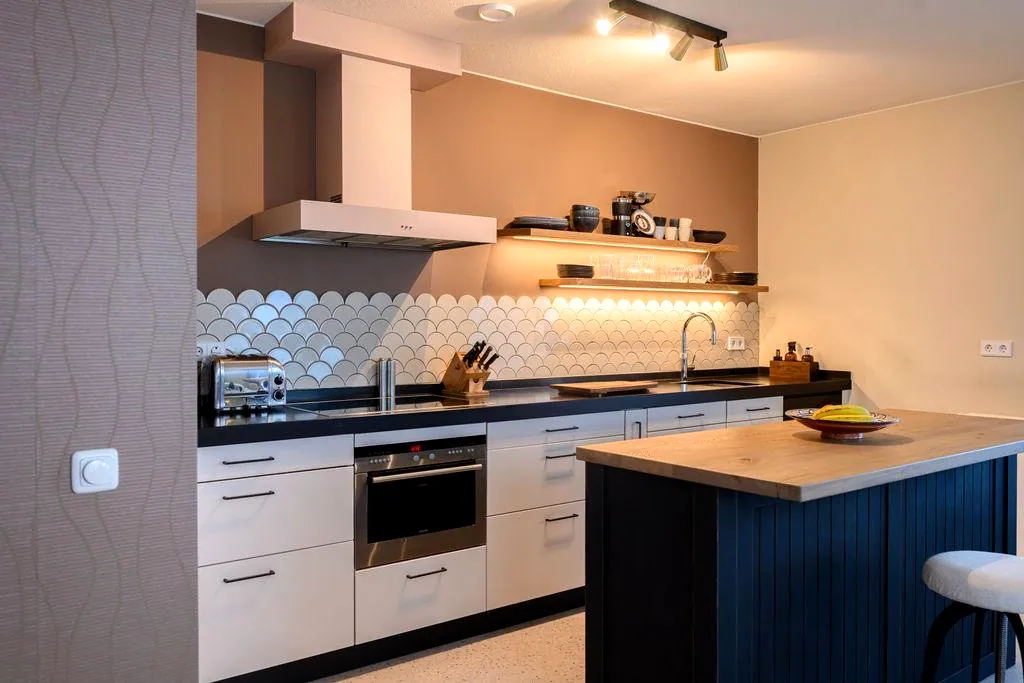 Keuken met lichtroze gewrapte fronten en afzuigkap, naast een donker kookeiland