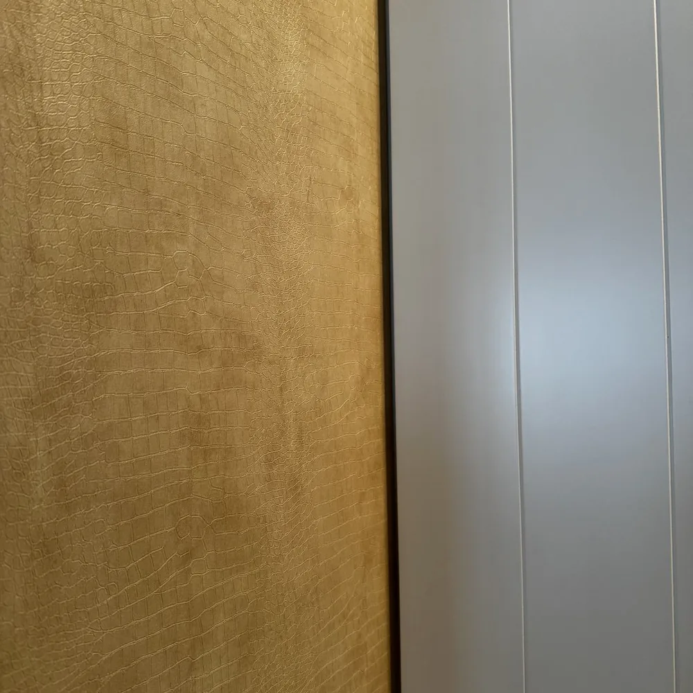 Close-up van de beige leather look met gouden glans naast een witte kastdeur