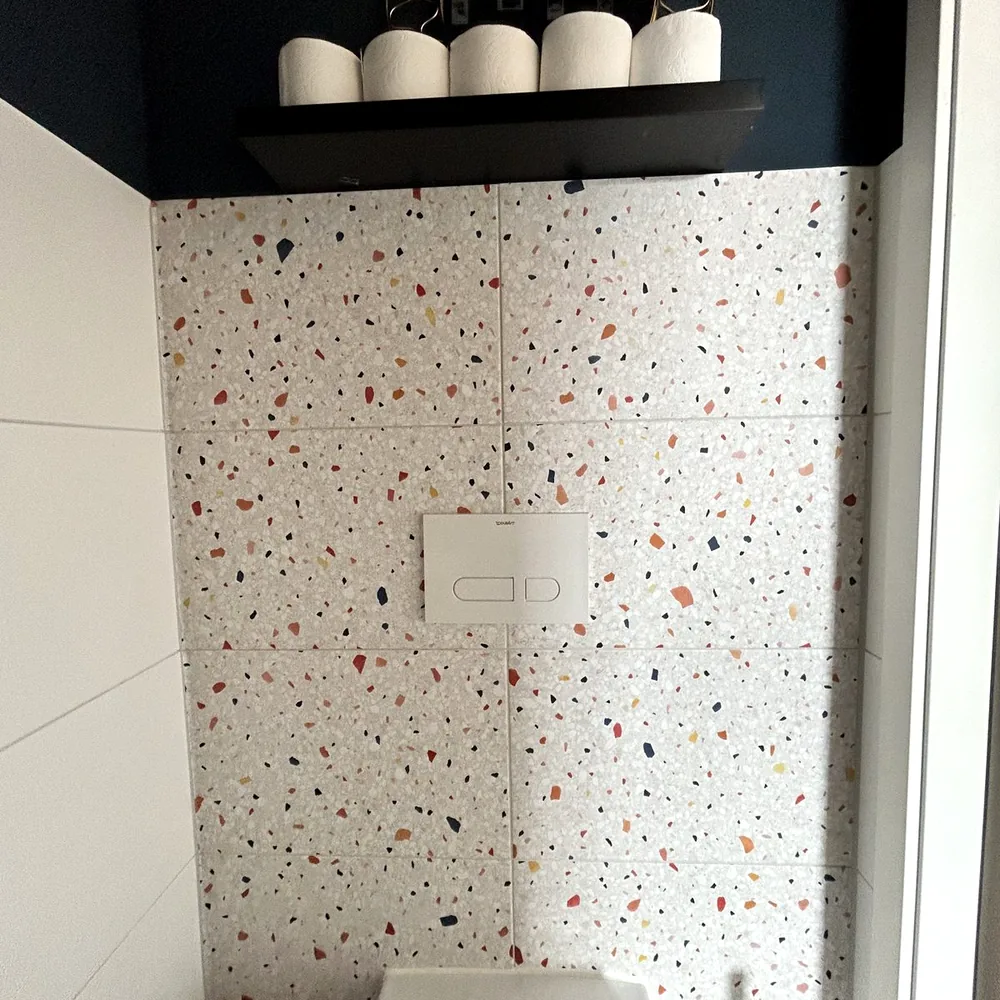 Toiletruimte met de tegelwand gewrapt in terrazzolook, onder een zwarte plank
