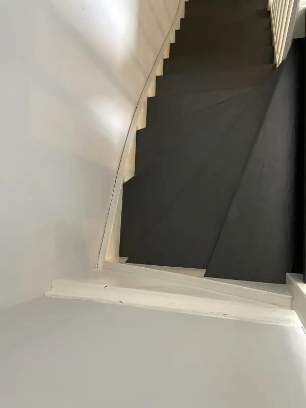 Trap met zwarte treden tussen witte wanden, van onderaf
