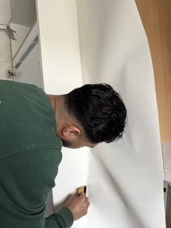 Monteur strijkt witte folie glad langs de rand van een wand
