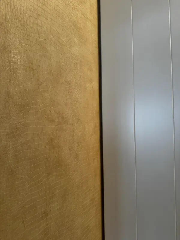 Close-up van de beige leather look met gouden glans naast een witte deur