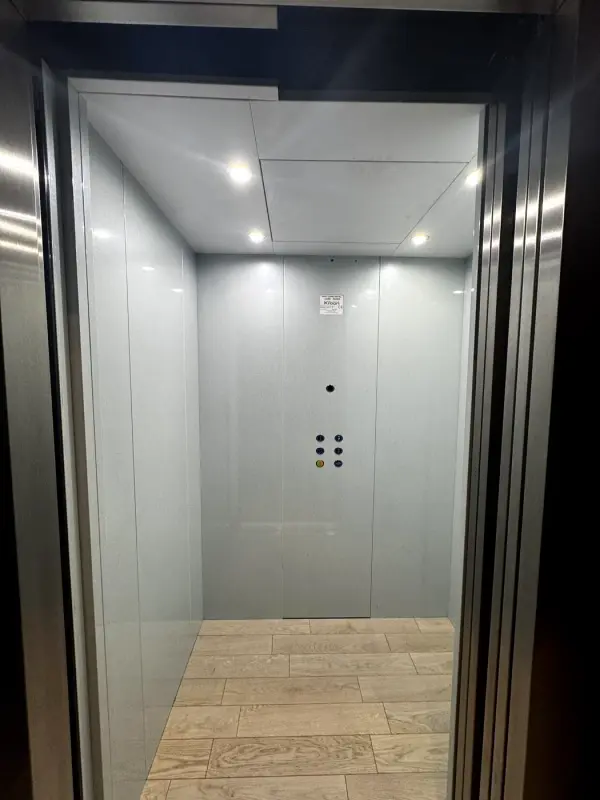 Voor: liftcabine met grijze wanden, vanaf de deur