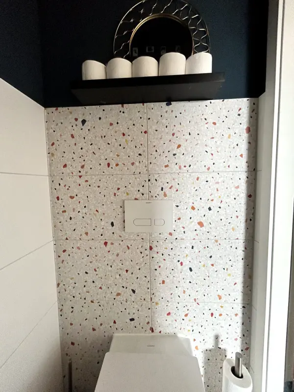 Na: toiletruimte met tegelwand in terrazzolook en hangend toilet