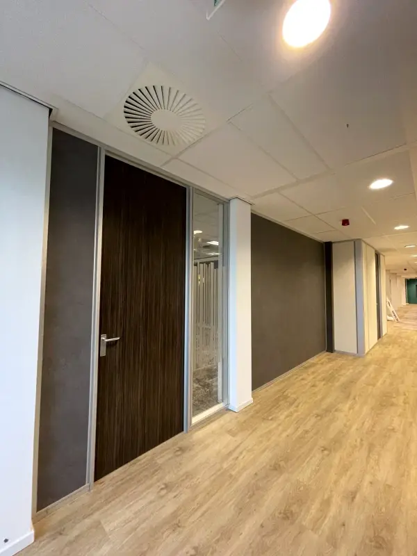Wand in donkere steenlook naast een gang en ramen